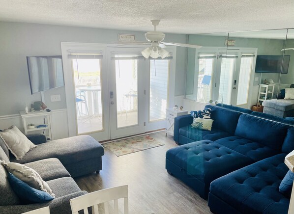 A spacious living room with a blue sofa set, a white chair, and a ceiling fan.