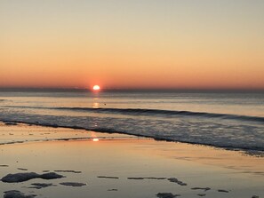 A beach scene with the sun setting over the ocean.