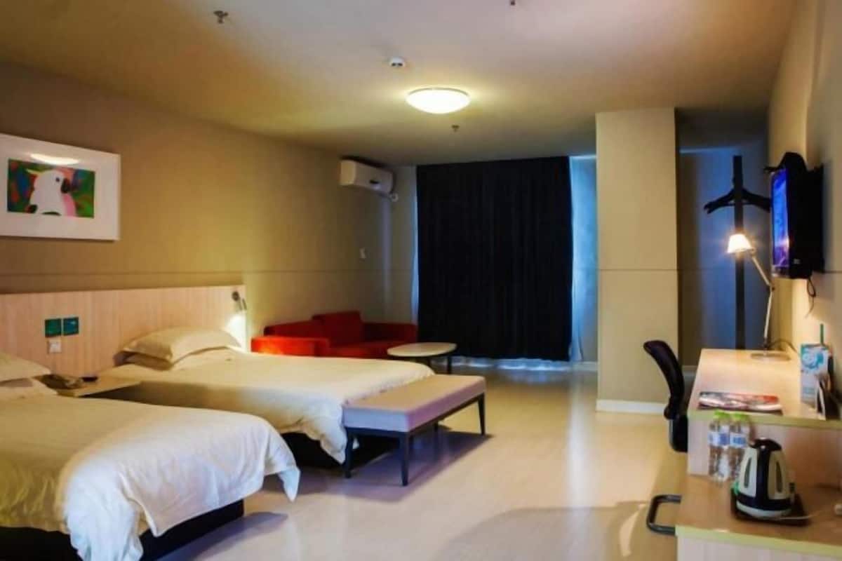 A hotel room with two beds, a red sofa, a small table, a TV, and a kettle.