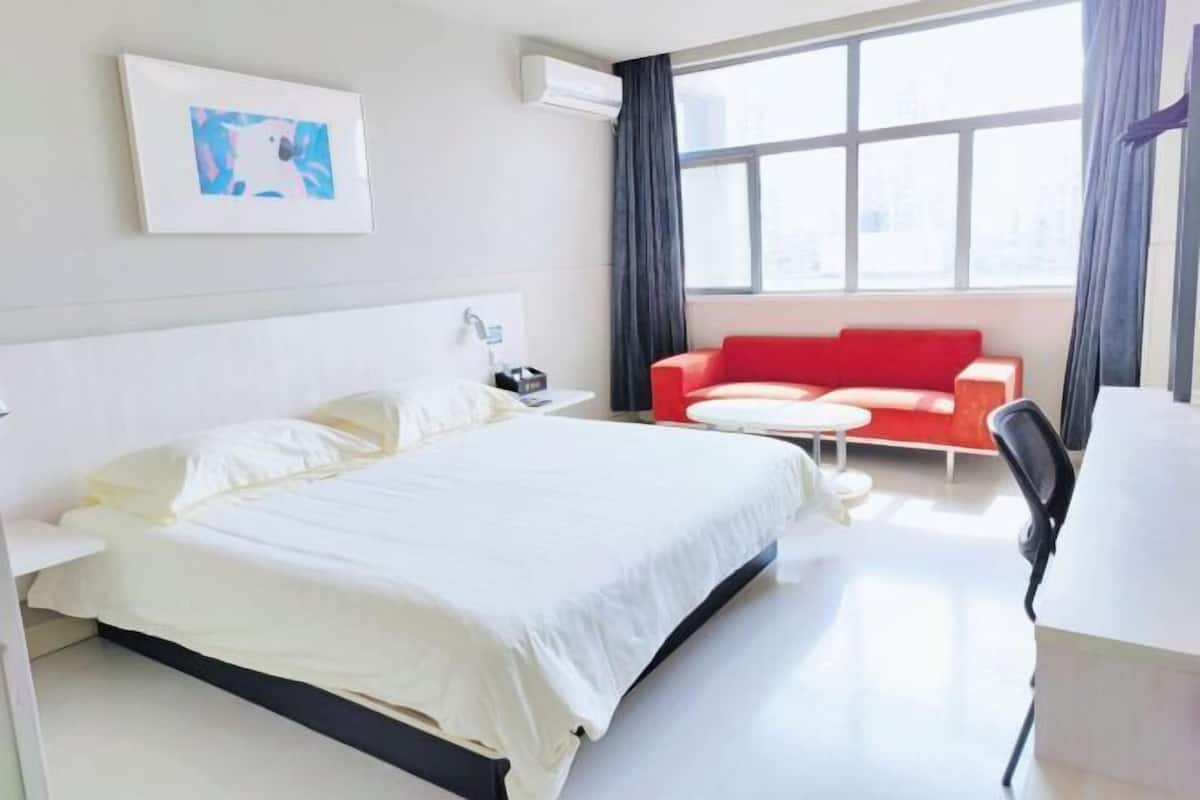 A hotel room with a bed, a red sofa, a small table, and a window with curtains.