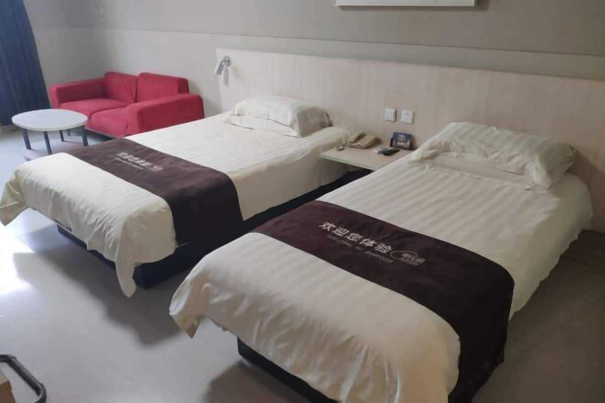 A hotel room with two beds, a red sofa, a small round table, and a bedside phone.