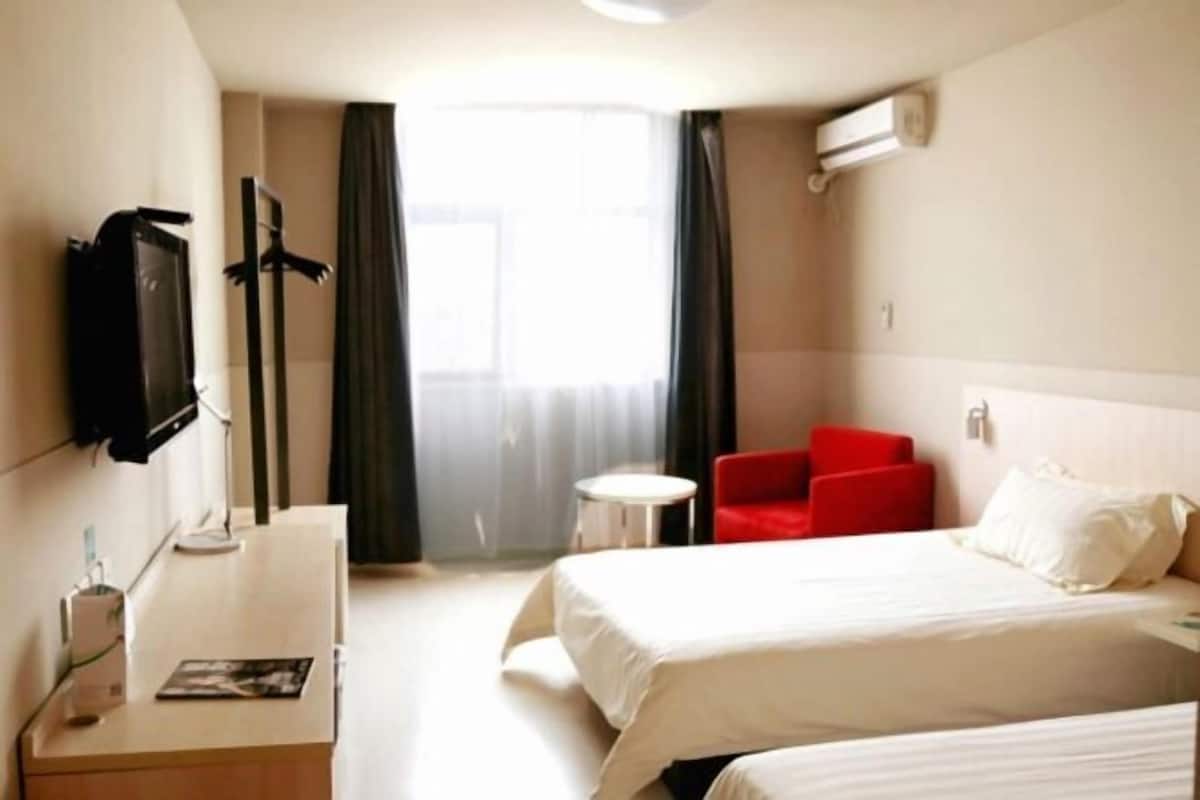 A hotel room with a bed, a desk with a chair, a TV, and a window with curtains.