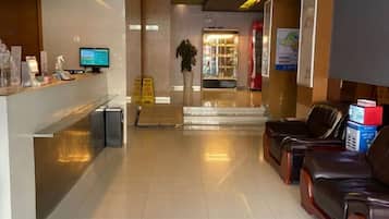 A hotel reception area with a reception desk, a computer monitor, a plant, and leather seating.