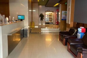 A hotel reception area with a reception desk, a computer monitor, a plant, and leather seating. - Jinjiang Inn (Lianyungang Xinpu Park Pedestrian Street) (Lianyungang)