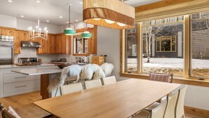 Une cuisine moderne avec des meubles en bois, une cuisinière en acier inoxydable et une grande fenêtre donnant sur un paysage enneigé.