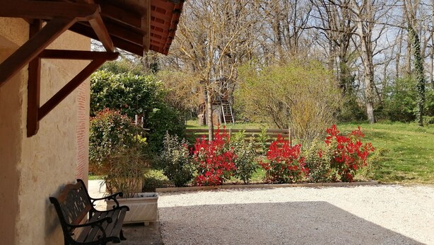 Un espacio de estar al aire libre cubierto con un banco, un sendero de grava y un jardín con flores rojas y árboles.
