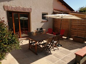 Une terrasse extérieure avec une table et des chaises en bois, un grand parasol et une clôture en bois.