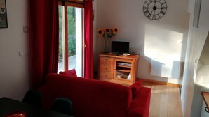 Una sala de estar con un sofá rojo, un mueble de televisión de madera con un televisor de pantalla plana, un reloj de pared y una ventana con cortinas rojas.