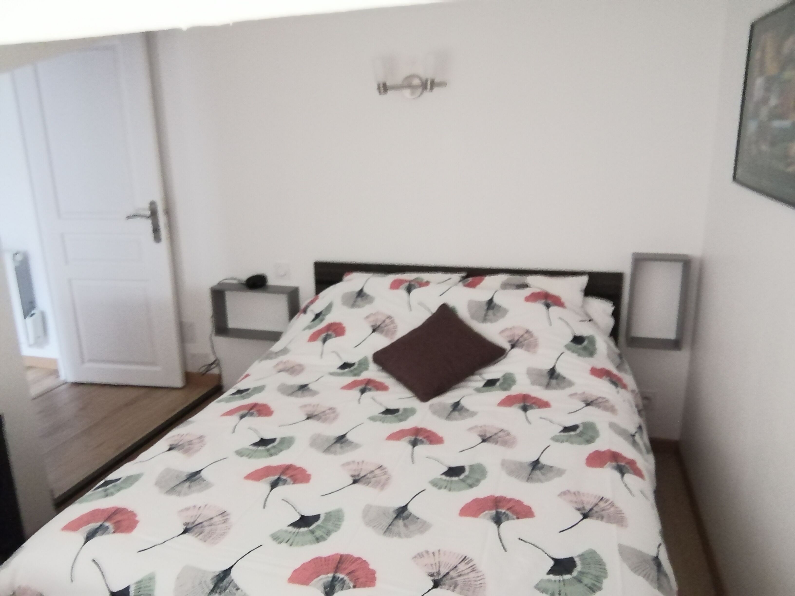 Quarto com cama, mesa de cabeceira, luminária na parede e porta.