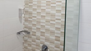Une douche avec une porte en verre, des carreaux beiges et blancs, une pomme de douche en chrome et un robinet en chrome.