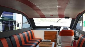 L'intérieur d'un bateau, avec des sièges à rayures, une table centrale et une vue sur l'eau à l'extérieur.