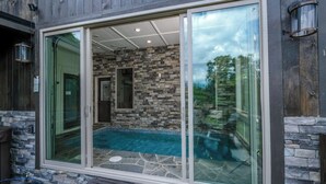Una casa moderna amb façana de pedra, una porta corredissa de vidre que dona a una zona de piscina i un banc de pedra a l'exterior.