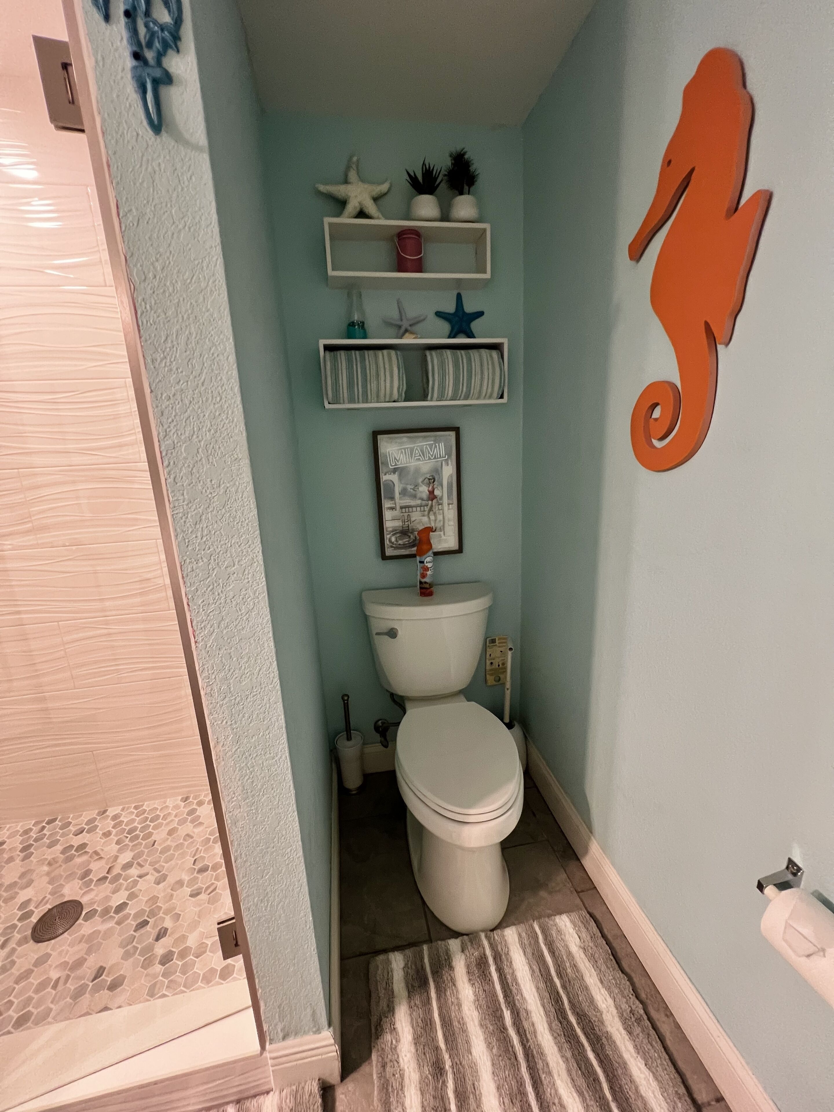 A bathroom with a toilet, a shower, a towel rack, and a decorative seahorse on the wall.