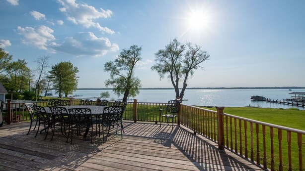 A wooden deck with outdoor furniture overlooking a lake, a grassy area, and a dock with a boat. - La Bella Vita: Spectacular Cayuga Lake Sunsets! (Cayuga)