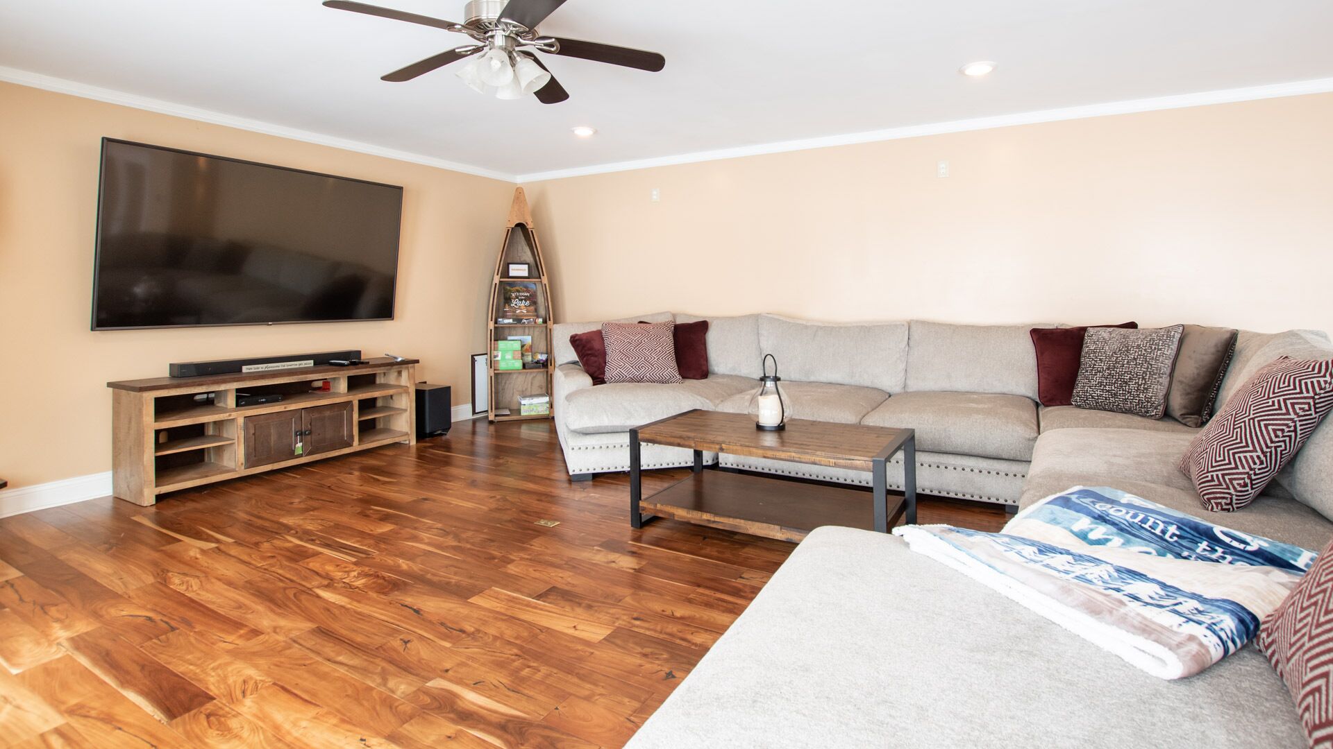 A spacious living room with a large flat-screen TV, wooden entertainment unit, and a ceiling fan.