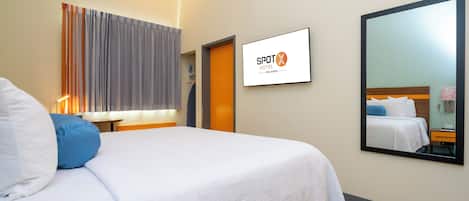 Une chambre d’hôtel avec un lit, un grand miroir, un téléviseur fixé au mur et une fenêtre avec des rideaux.