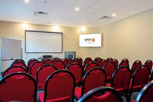 A conference room with rows of red chairs, a whiteboard, a projector screen displaying 'SPOT HOTEL ORLANDO', and a flat-screen TV.