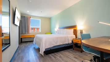A hotel room with a bed, bedside tables, a desk, a chair, a mirror, and a window with curtains.