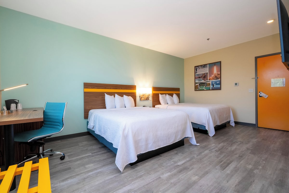 A hotel room with two beds, a desk, a chair, and a door.