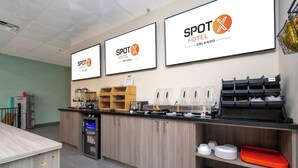 A hotel reception area with a counter, coffee machines, and a refrigerator. - SPOT X Hotel Orlando/Intl Dr by The Red Collection (Orlando)