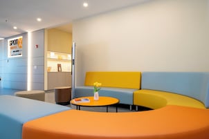 Een hotel lobby met een receptiebalie, een zithoek met een gele bank en een ronde tafel, en een muur met een bord met daarop Spot Hotel Orlando.