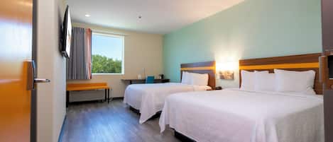 Une chambre d’hôtel avec deux lits, un bureau, une chaise, une fenêtre avec des rideaux et un téléviseur à écran plat fixé au mur.