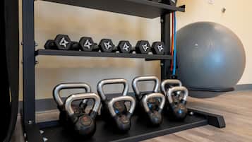 A gym with weightlifting equipment including dumbbells and kettlebells on racks.