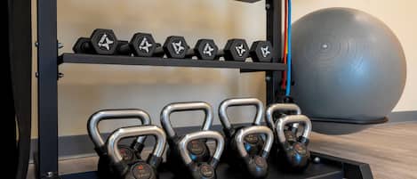 A gym with weightlifting equipment including dumbbells and kettlebells on racks.