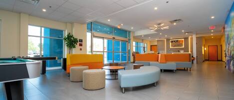 A spacious lobby with a pool table, comfortable seating areas, and a reception desk.