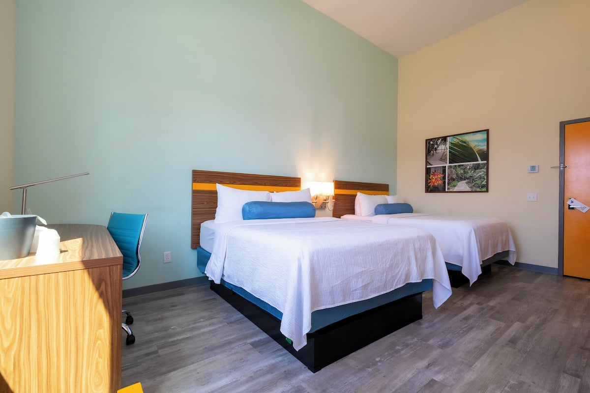 A hotel room with two beds, a desk, and a chair.