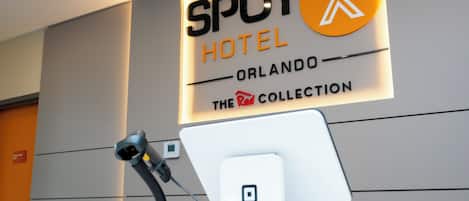 Ein Empfangsschalter mit einem digitalen Bildschirm, einem Headset und einem Schild mit der Aufschrift 'SPOT HOTEL ORLANDO THE COLLECTION'.