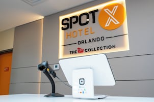 Een receptiebalie met een digitaal scherm, een headset en een bord met de tekst 'SPOT HOTEL ORLANDO THE COLLECTION'.
