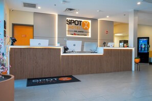 A hotel reception desk with multiple HP computers, a digital screen, and a reception area with a wooden finish. - SPOT X Hotel Orlando/Intl Dr by The Red Collection (Orlando)