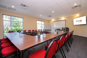 Un salón de conferencias con una larga mesa, sillas rojas, una pantalla de proyector y una pizarra.
