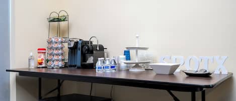 A kitchenette with a coffee maker, water bottles, a coffee dispenser, and a cake stand.