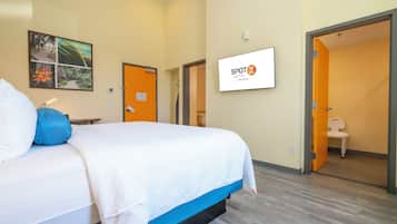 A hotel room with a bed, a television, and a door leading to a bathroom.