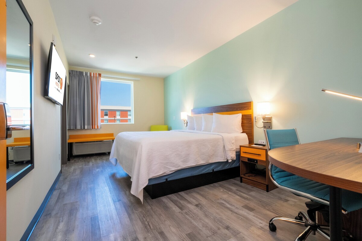 A hotel room with a bed, bedside table, lamp, chair, and a small table.