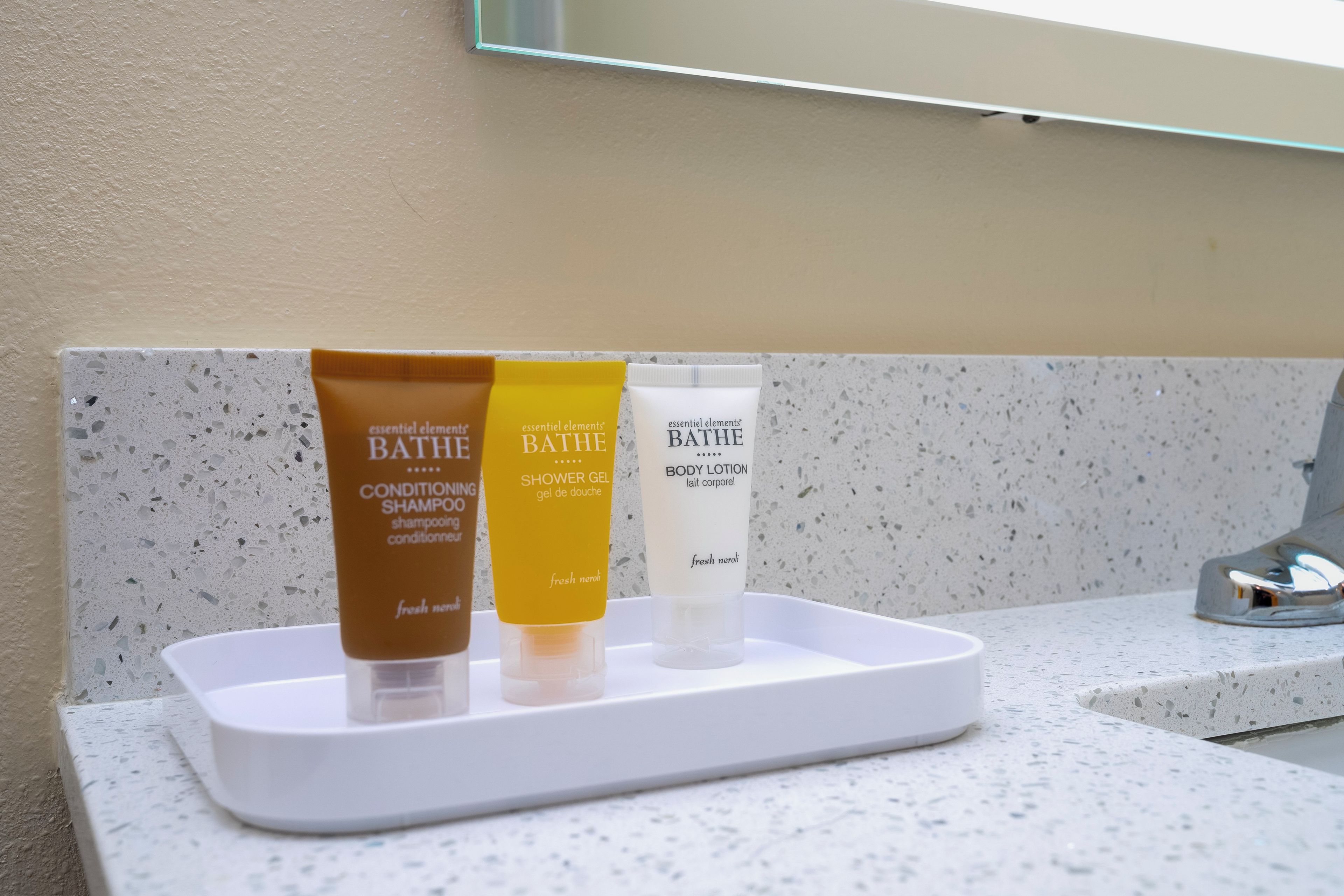 Una encimera de baño con tres artículos de aseo: una botella marrón de champú, una botella amarilla de gel de ducha y una botella blanca de loción corporal.