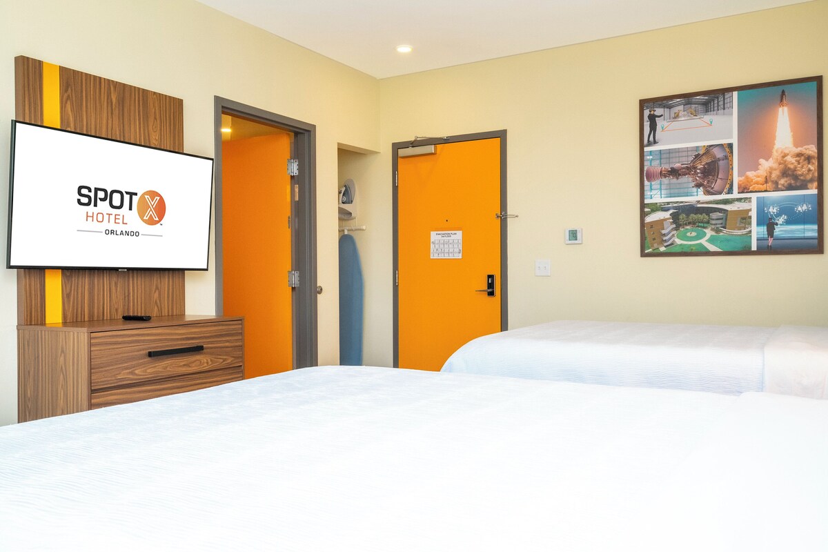 A hotel room with two beds, a TV mounted on the wall, and a framed collage on the wall.