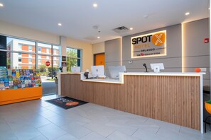 A hotel reception desk with a digital display, a wooden reception area, and a view of the outside. - SPOT X Hotel Orlando/Intl Dr by The Red Collection (Orlando)