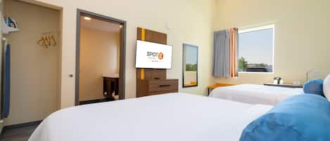 A hotel room with two beds, a TV, a mirror, and a window with curtains.