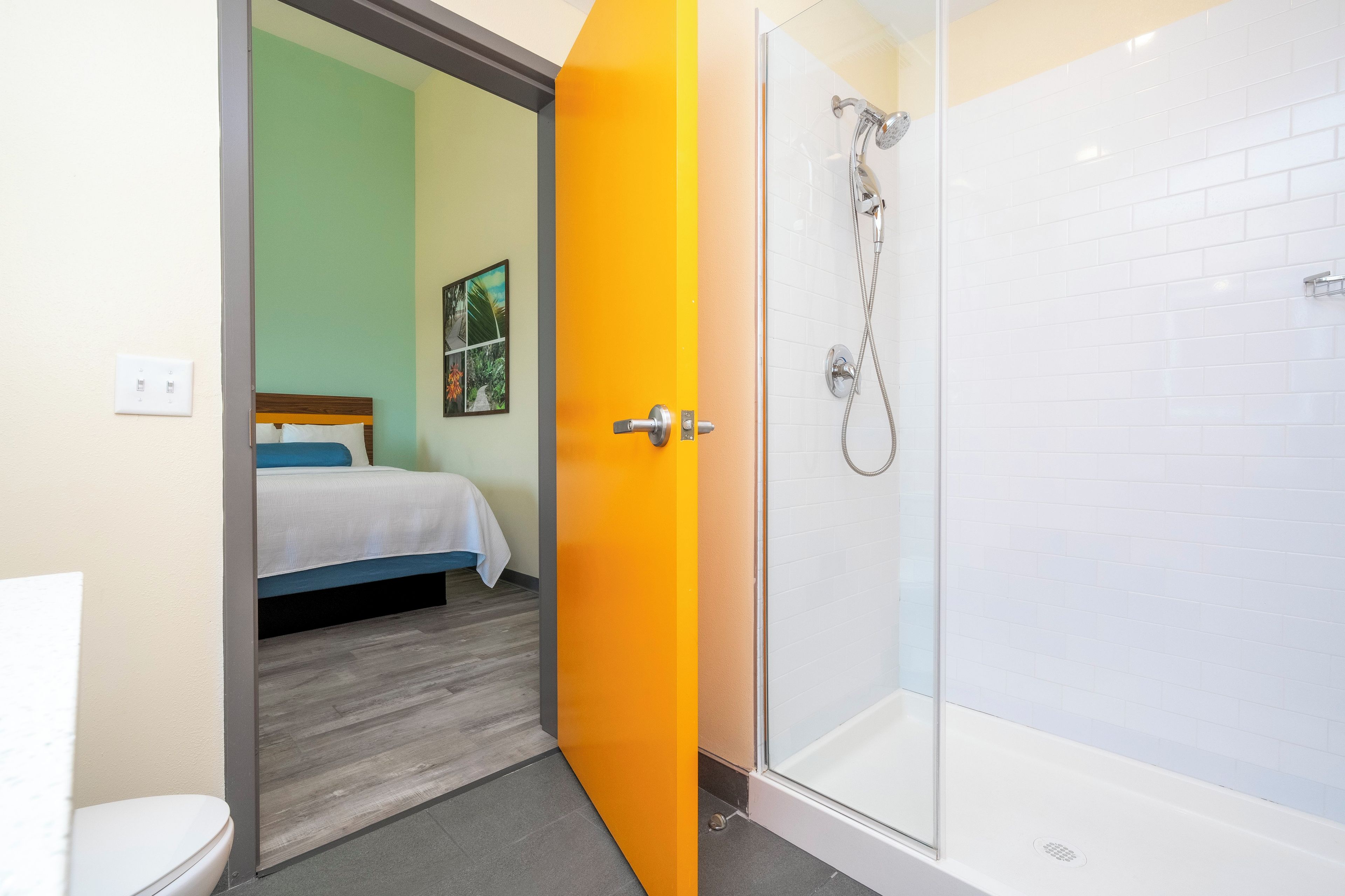 Ein Badezimmer mit Dusche, Toilette und einem Bett, das eine grüne Wand und ein Bild zeigt.