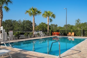 A swimming pool with a metal ladder, surrounded by lounge chairs and a fence. - SPOT X Hotel Orlando/Intl Dr by The Red Collection (Orlando)