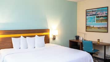 Habitación de hotel con cama, escritorio, silla y lámpara de pared.