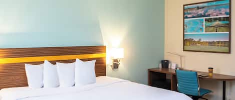A hotel room with a bed, a desk, a chair, and a wall-mounted lamp.