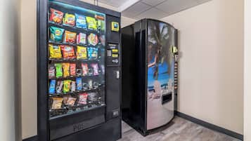 A vending machine with snacks and a refrigerator with a tropical mural.