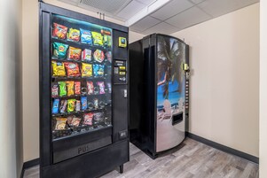 A vending machine with snacks and a refrigerator with a tropical mural.