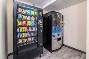 Máquina expendedora con aperitivos y un refrigerador con un mural tropical.