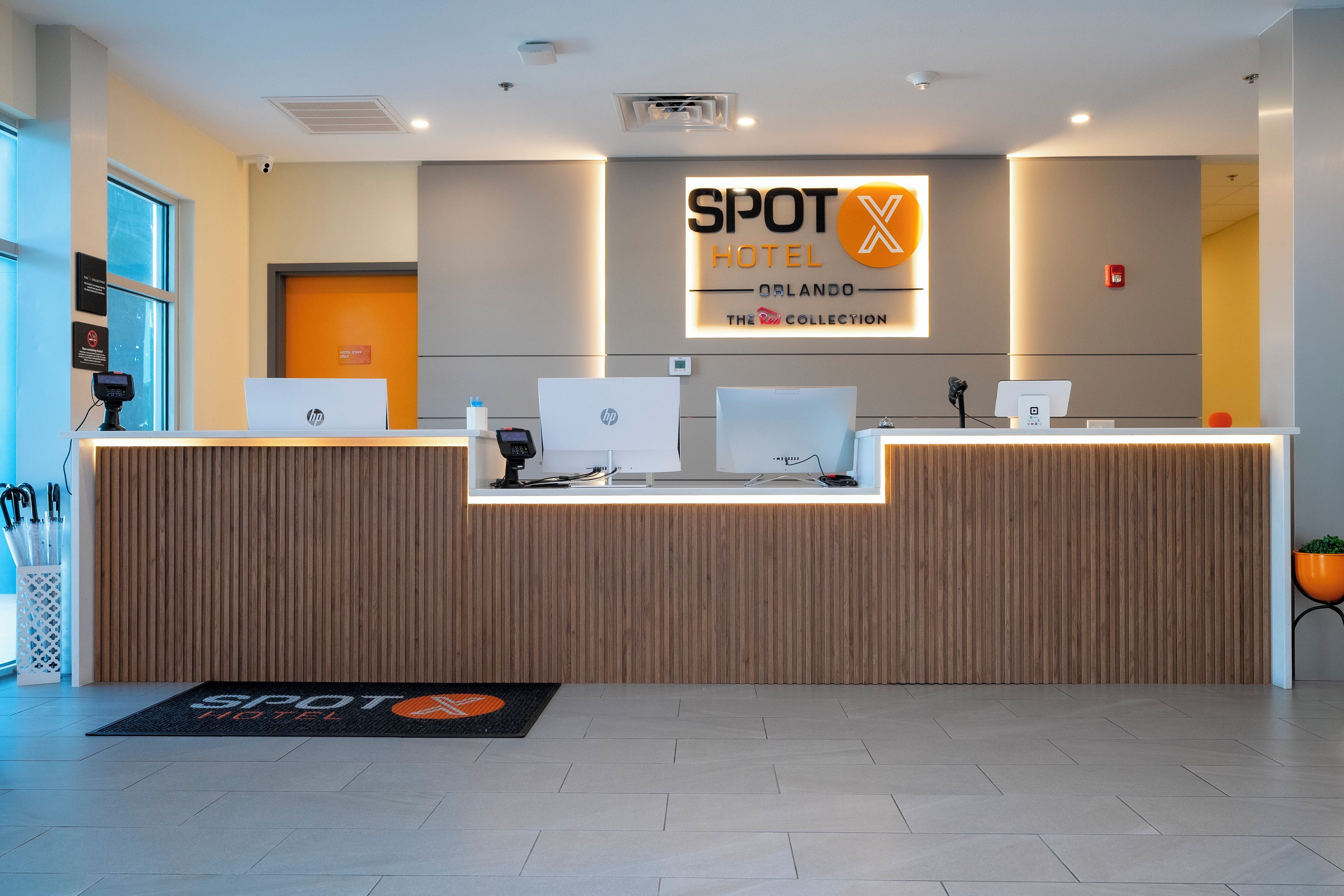 Un comptoir d’accueil d’hôtel équipé d’ordinateurs HP, d’un écran numérique et d’une enseigne indiquant « SPOT HOTEL ORLANDO ».