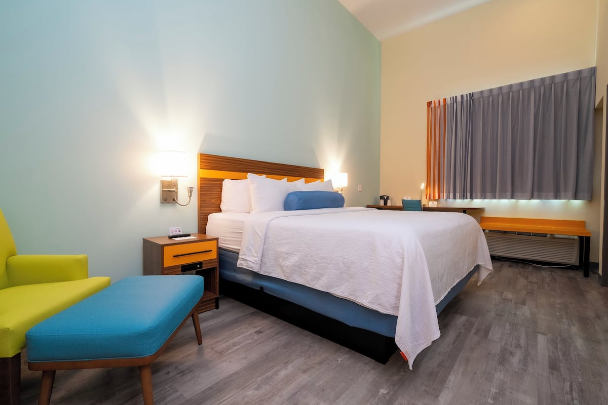 A hotel room with a bed, a bedside table, a chair, and a bench.